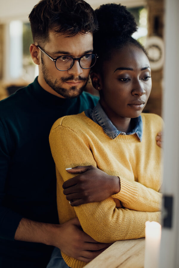 Young pensive couple embracing while feeling worried about something at home.