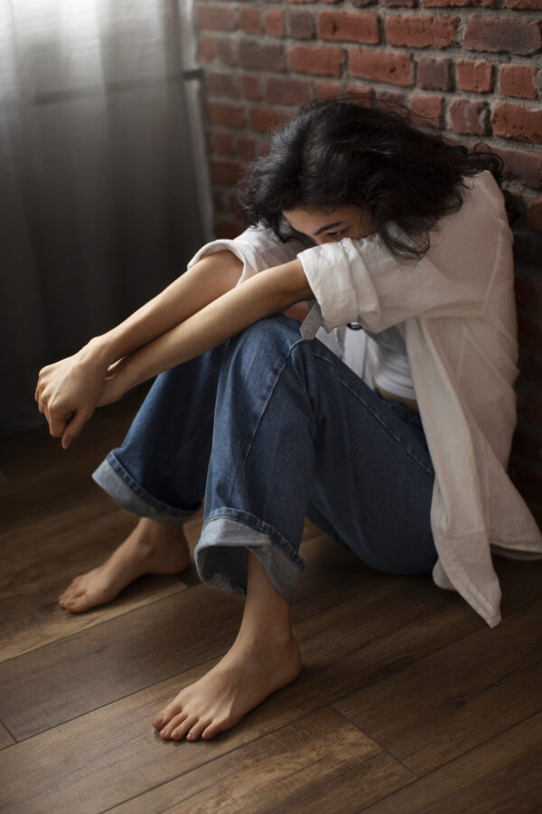 young woman sitting on ground with arms folded anxiously