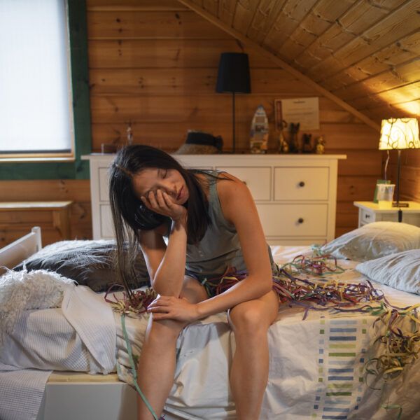 woman in bed rubbing eyes hungover and tired hovering over pizza boxes