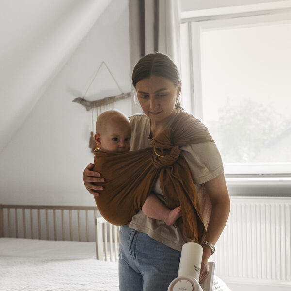 woman cleaning with vaccuum while holding baby in sling