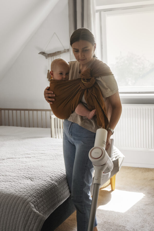 woman cleaning with vaccuum while holding baby in sling