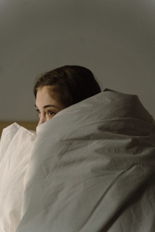 woman hiding in blanket covers with anxiety about sleep