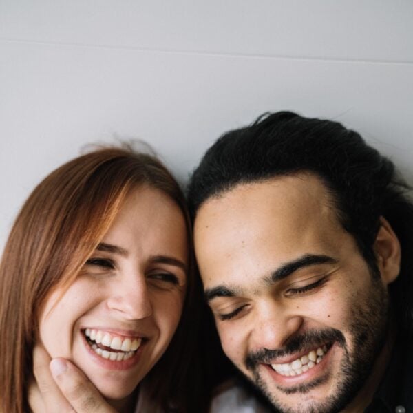 Two people smiling and leaning their heads together in a close-up portrait.